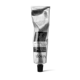 Un tubetto argentato e sgualcito di Resurrection Aromatique Hand Balm di Aesop, in piedi sul tappo nero, su sfondo bianco.