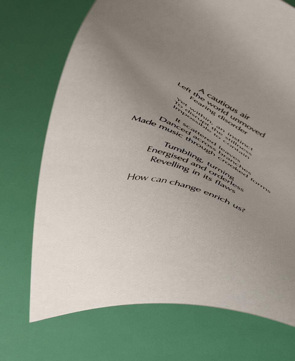 Carta color crema incurvata, con testo poetico, su uno sfondo verde tenue.