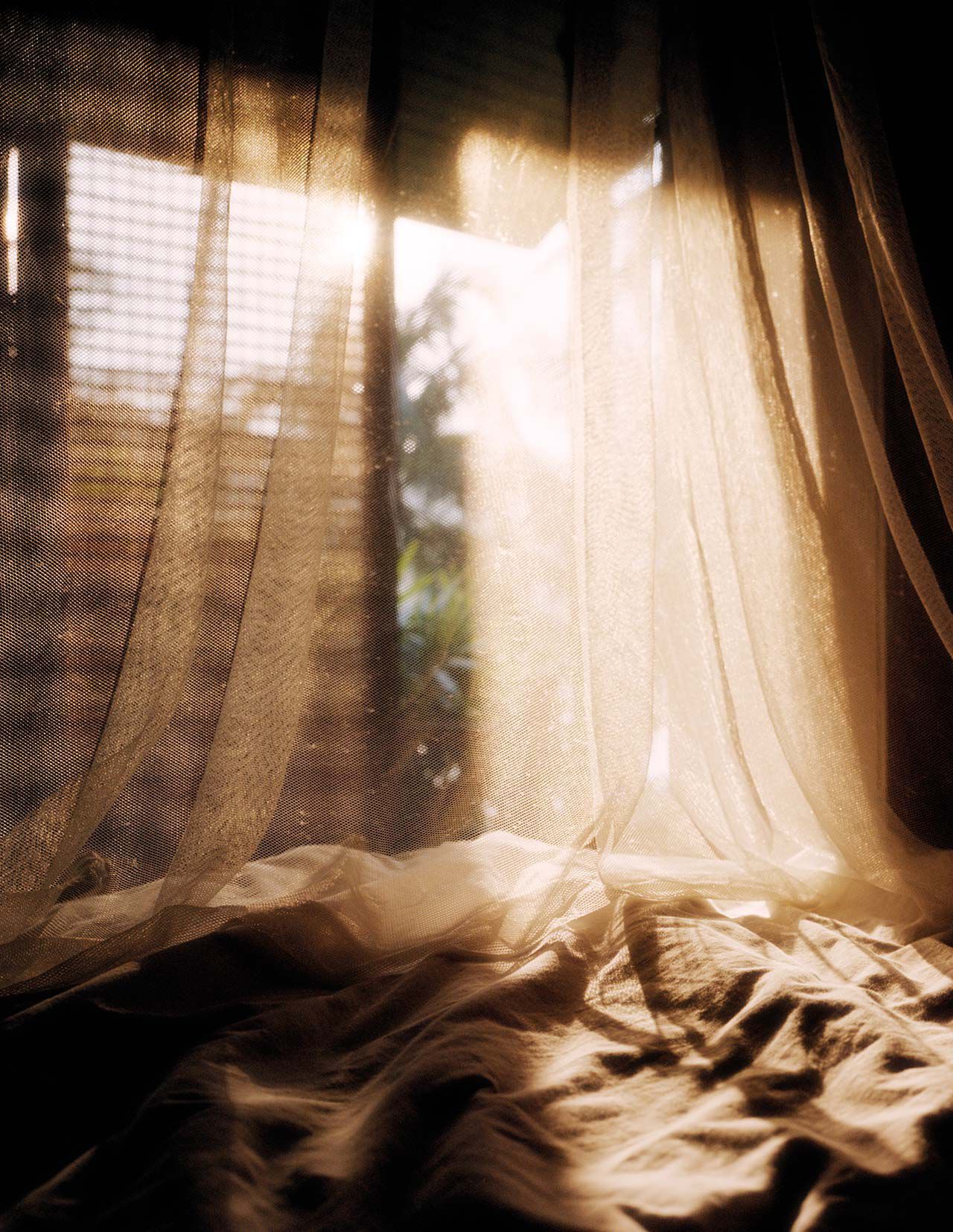 Tende leggere drappeggiate su tessuto stropicciato accanto a una finestra illuminata dal sole, in calde tonalita beige, con ombre morbide e pieghe traslucide.