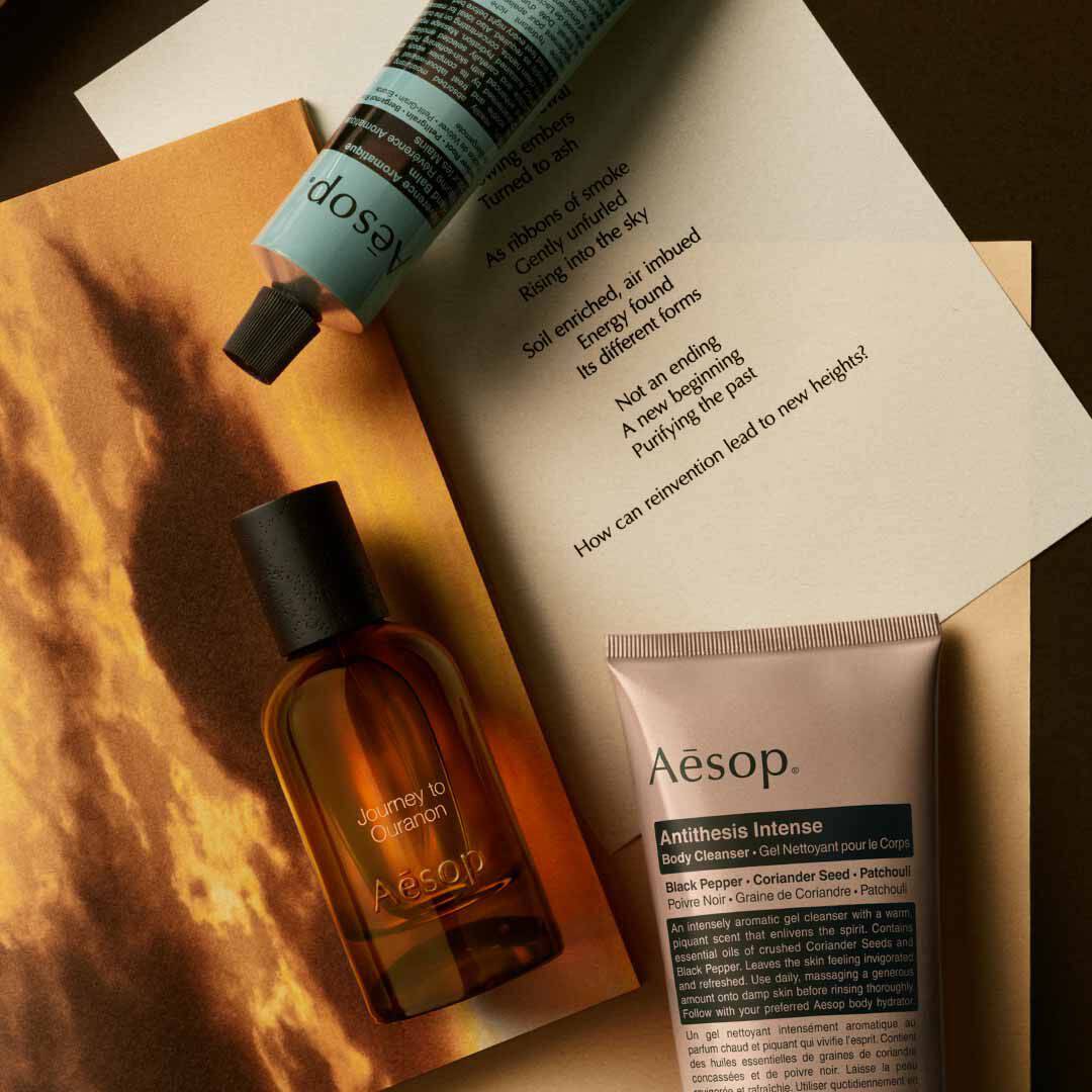 Flacone Aesop Journey to Ouranon con flacone a pompa e tubo, disposti su fogli con un’immagine di paesaggio luminoso.