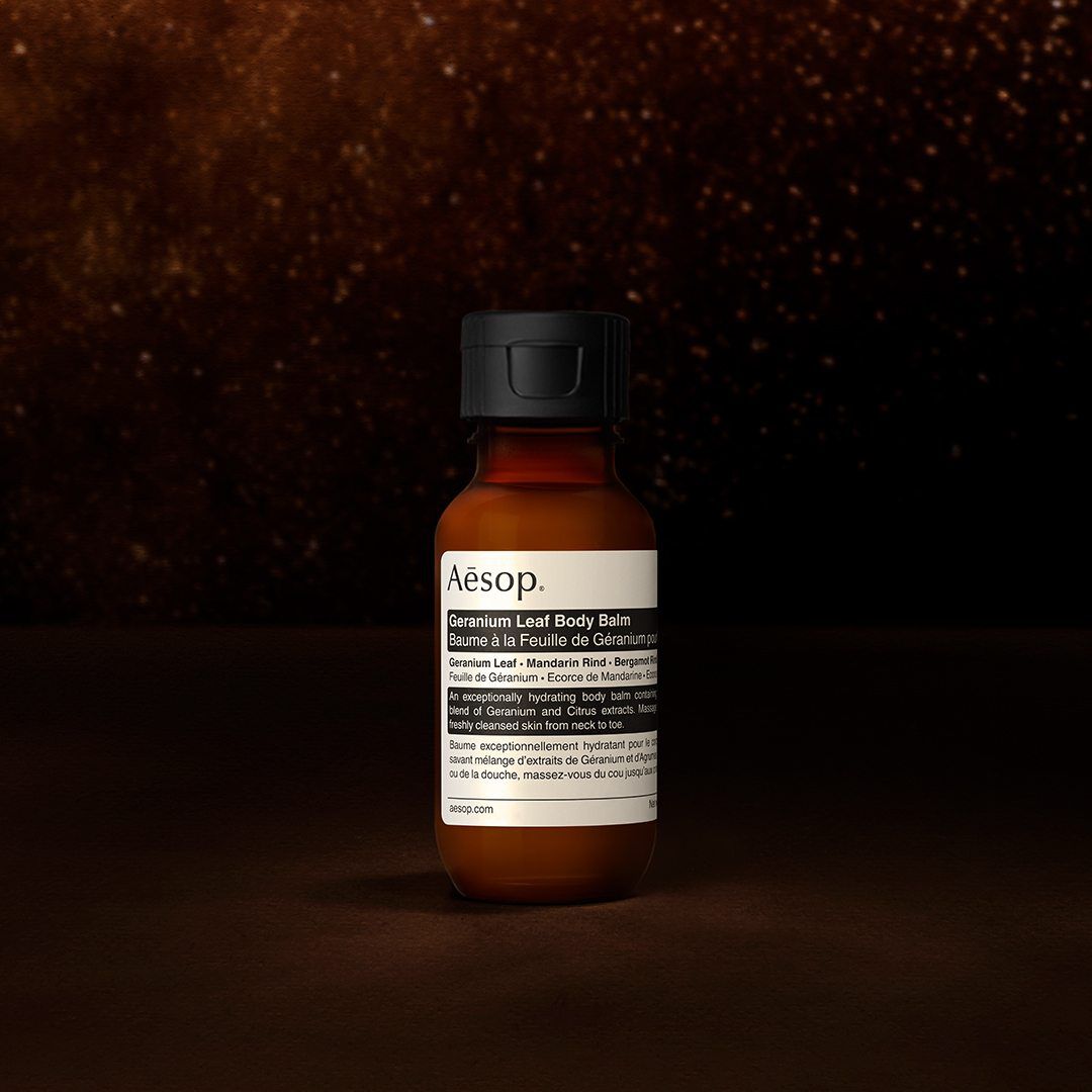 Un flacone di balsamo corpo Geranium Leaf di Aesop su sfondo scuro e strutturato.
