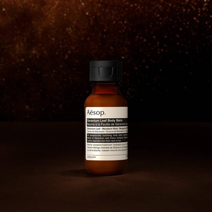 Un flacone di balsamo corpo Geranium Leaf di Aesop su sfondo scuro e strutturato.