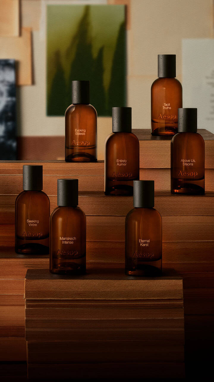 Flaconi di profumo in vetro ambrato Aesop esposti su libri impilati.
