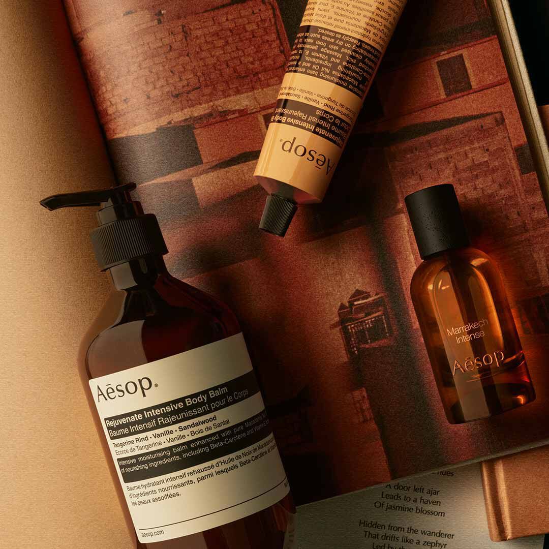 Flacone Aesop Marrakech Intense con flacone a pompa e tubo giallo, disposti su fogli dai toni caldi.