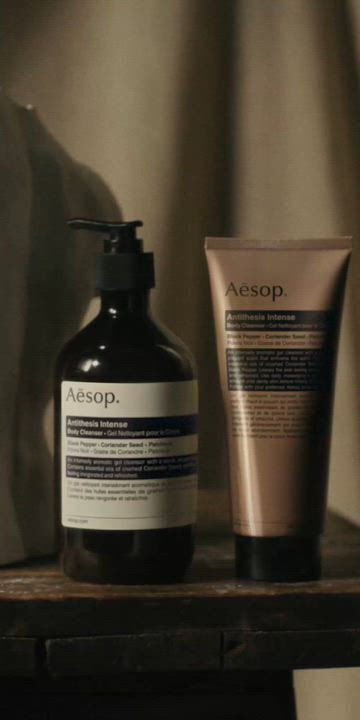 Aesop Antithesis Intense Body Cleanser pump bottle and tube beside a white torso sculpture on a wooden work table.