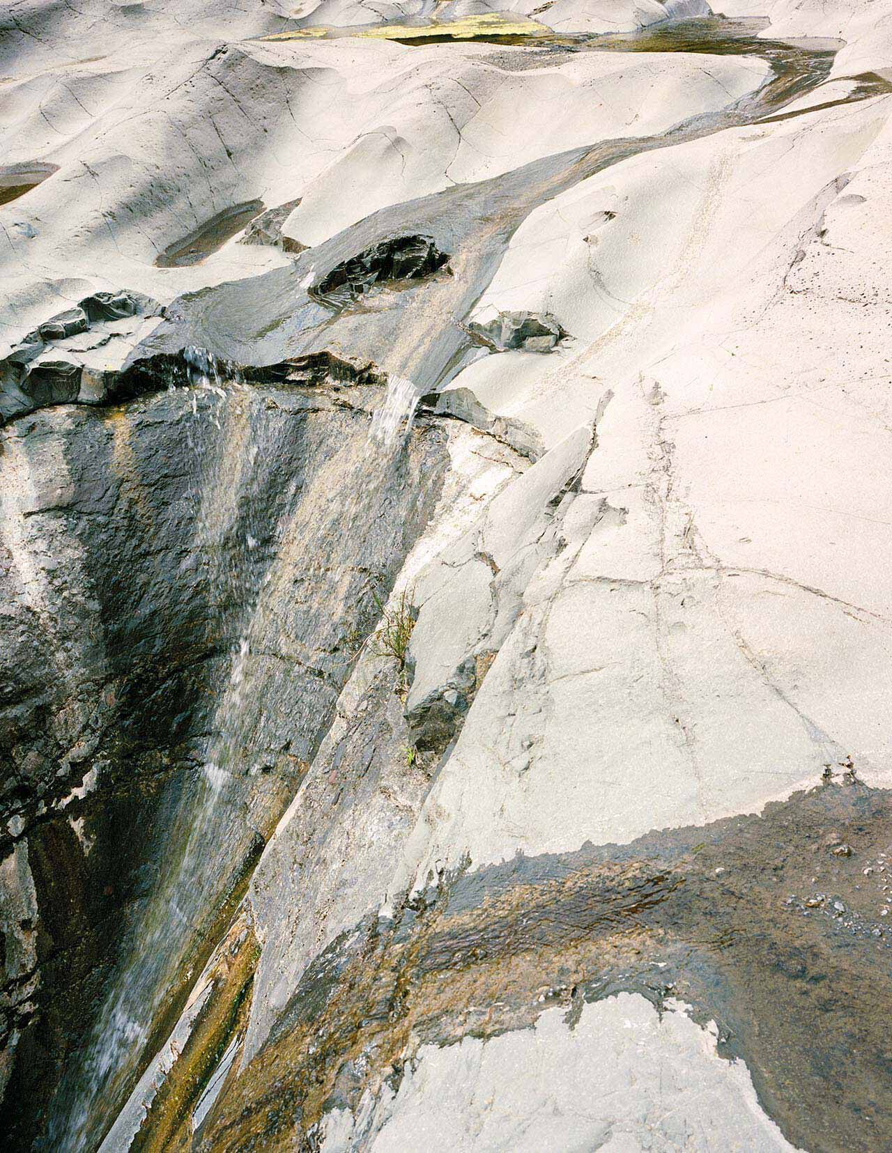 Superficie minerale in pietra chiara, con venature bianche, grigie e antracite, texture stratificate e una frattura diagonale che attraversa l’inquadratura.