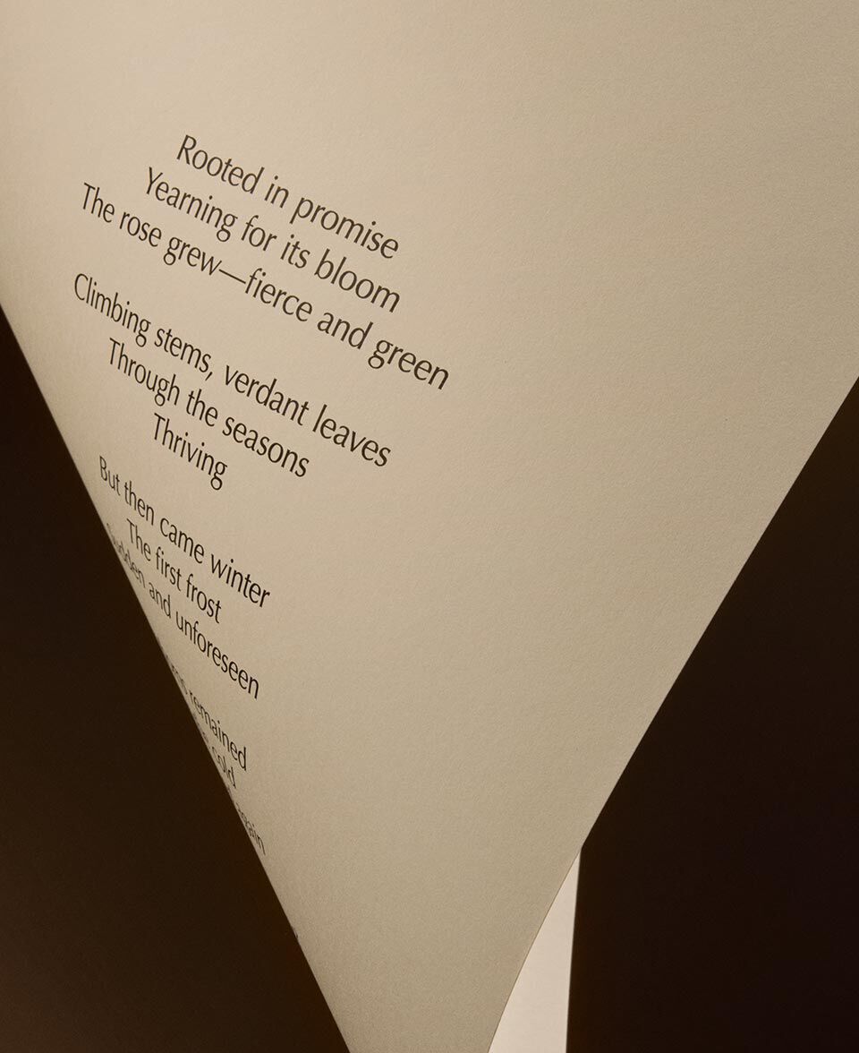 Piega triangolare di carta color crema, con il testo di una poesia su fondo scuro.