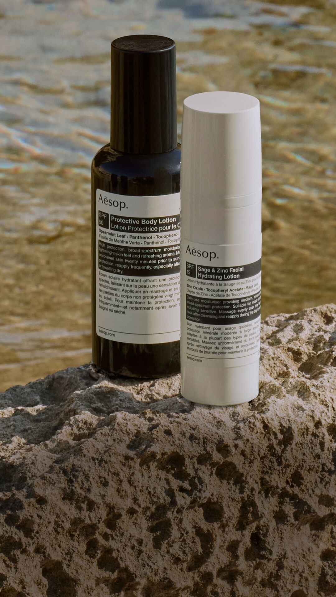 Un'accurata selezione di formulazioni per la protezione solare Aesop adagiate su una roccia in riva al mare.